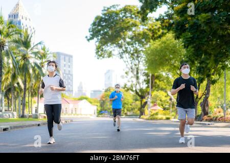 Asiatische junge drei Frauen und Männer joggen und exciseing im Stadtpark und tragen Schutzmaske im Gesicht für fit bleiben während Covid-19 Pfanne Stockfoto