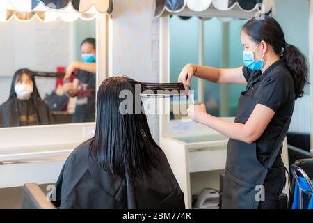 Asiatische junge Frau trägt Gesichtsmasken, um sich von Covid-19 während Friseur Schneiden schwarzen Haaren mit Schere im Schönheitssalon zu schützen. Stockfoto