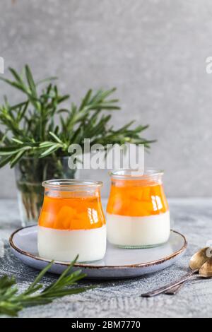 Hausgemachte Panna Cotta mit Scheiben von Pfirsich und Pfirsich Gelee in Glasgefäßen auf einem grauen Beton Hintergrund. Stockfoto