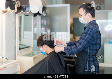 Asiatischer junger Mann und Friseur Mann trägt medizinische Maske, um sich während des Novel Coronavirus zu schützen, Covid-19 in Barbershop Hair Care Service. Stockfoto