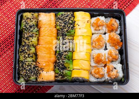 Set von Brötchen Sushi mit Lachs und Gemüse in schwarzem Tablett auf roter Korbmatte. Ein japanisches Gericht mit Meeresfrüchten Stockfoto