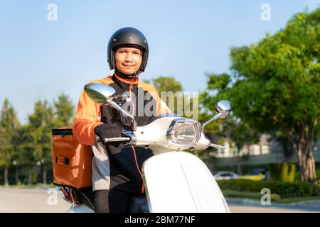 Asian man Kurier auf Roller, der Lebensmittel in den Straßen der Stadt mit einer heißen Lieferung von Speisen von der Mitnahme und Restaurants nach Hause liefert, Express Food Delivery a Stockfoto