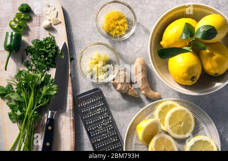 Sommerzutaten, frische grüne und gelbe Gewürze und Aromen. Petersilie, Zitrone, Knoblauch, grüne Chili und Ingwer. Rustikale Szene auf einem sonnigen Tisch. Altern Stockfoto