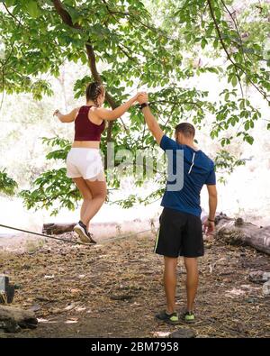 Junge Menschen, die Slacklining ist eine Praxis in Balance, die in der Regel Nylon oder Polyester Gurtband zwischen zwei Ankerpunkten gespannt verwendet. Stockfoto