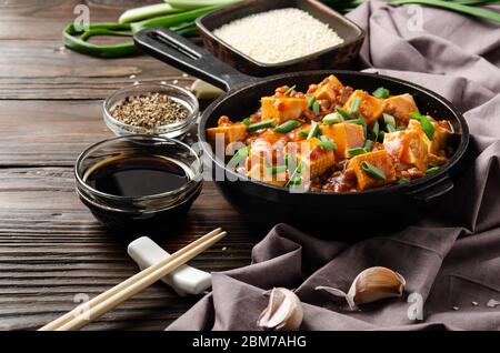 Mapo Tofu in Gusseisen Pfanne mit Schweinefleisch gehackten Schnittlauch Sojasauce sichuan Pfeffer Knoblauch und Gewürze Nahaufnahme auf Holztisch Stockfoto