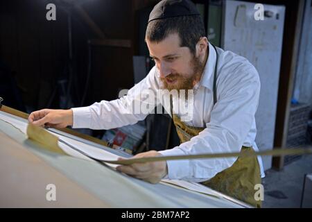 Ein Rabbi und Meister schneidet ein neues Pergament, das in seiner Kellerwerkstatt hergestellt wurde und für religiöse Gegenstände verwendet werden soll. Stockfoto