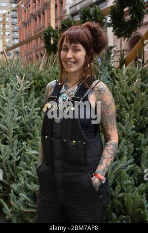 Eine hübsche Schottin mit Tattoos, die an einem milden Dezembertag Weihnachtsbäume auf dem Astor Place in Greenwich Village, Manhattan, New York City verkauft. Stockfoto