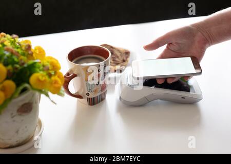 Kontaktlose Bezahlung über Mobiltelefon im Café. Kunden zahlen am POS-Terminal am Schalter im Café. Stockfoto