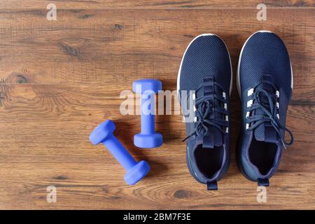 Sportschuhe und Hanteln auf Holzhintergrund Draufsicht. Fitnesskonzept. Kopierbereich. Stockfoto