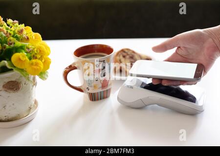 Kontaktlose Bezahlung über Mobiltelefon im Café. Kunden zahlen am POS-Terminal am Schalter im Café. Stockfoto