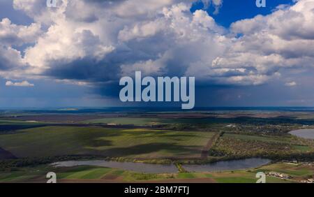 Große Sturmwolken, unter denen es sintflutartigen Regen mit Blitz, über landwirtschaftlichen Feldern. Blick von der Drohne Stockfoto