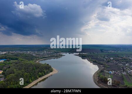 Große Sturmwolken, unter denen es sintflutartigen Regen mit Blitz, über landwirtschaftlichen Feldern. Blick von der Drohne Stockfoto
