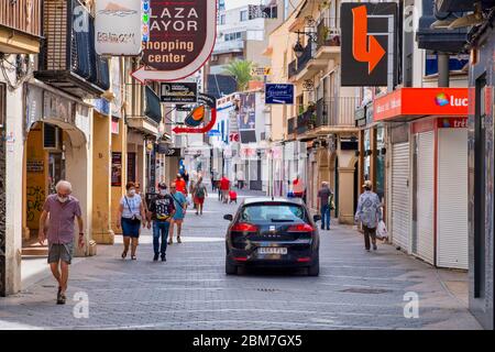 Benidorm, Alicante, Spanien, 4. Mai 2020, Corona Krise: Polizeifahrzeuge patrouilliert, während nur wenige Einwohner auf dem Weg zum oder vom Einkaufen in einer normalerweise belebten Fußgängerzone in der Altstadt zwischen Geschäften mit geschlossenen Fensterläden laufen Stockfoto