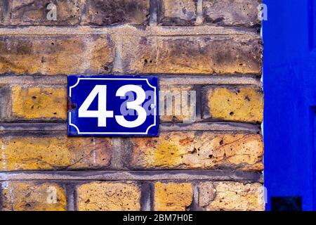 Haus Nr. 43 auf einem blauen E-Mail-Schild an einer Ziegelwand neben einer blauen Eingangstür Stockfoto