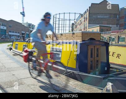 Ein junger Mann fährt an einem schmalen Boot auf dem Schlepptweg des Regents Canal in der Nähe des Broadway Market in Hackney, East London, an einem sonnigen Morgen vorbei Stockfoto