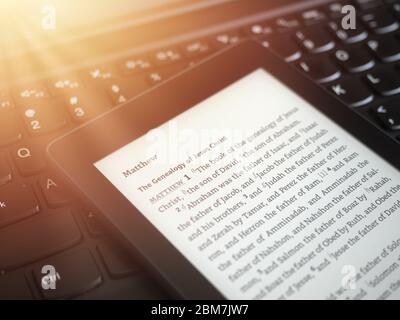 Nahaufnahme des ebook Lesers mit der Heiligen Bibel auf einer Laptop-Tastatur, mit Sonnenstrahlen Licht Konzept Stockfoto