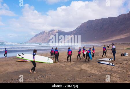 Surfer mit Surfbrettern am Strand in der beliebten Wassersportstation Caleta de Famara auf Lanzarote, Kanarische Inseln Stockfoto