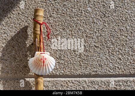 Stock und Muschel des Camino de Santiago auf Granitsteinmauer lehnend. Santiago de Compostela Pilgerfahrt Konzept Stockfoto