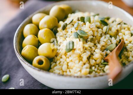 Bulgur mit grünen Oliven und Pepitas, gesunde Ernährung einfach Rezept aus lange gelagerten Lebensmitteln. Stockfoto