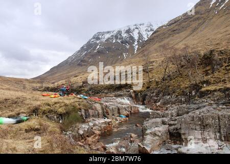 Gruppe von Universitätskajakfahrern, die einen Schnellboot auf dem Fluss Etive, Glen Coe, schottische Highlands, Schottland, Großbritannien, portieren Stockfoto