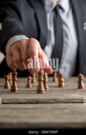 Geschäftsmann spielt eine Partie Schach auf einem alten Holztisch in einer Nahaufnahme seiner Hand erreichen schwarzen König Stück in einem konzeptionellen Bild von persönlichen Stockfoto