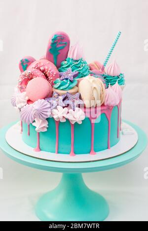 Rosa und türkisfarbene Torte mit Makronen, Cupcakes, Cake Pops, Baiser, Eiszapfen und geschmolzener Schokolade. Türkisfarbenes Cakestand, weißer Hintergrund Stockfoto