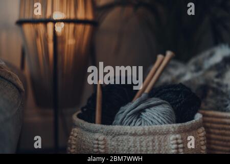 Nahaufnahme eines Korbes voller Garn im Inneren eines Hauses, mit großen Holz-Stricknadeln und Häkelnadel, flacher Fokus. Stockfoto