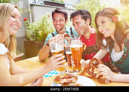 Lachende Freunde im Biergarten in Bayern klirrrend auf Gläser Bier Stockfoto