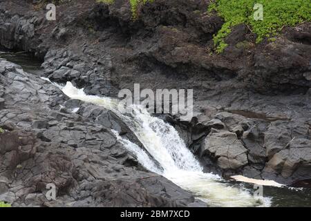 Palikea Bach läuft durch vulkanisches Gestein mit Scaevola taccada wächst auf dem Gestein am Oheo Gulch in Hana, Maui, Hawaii, USA Stockfoto