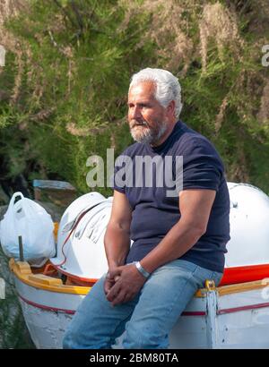 Der reife Fischer ruht auf seinem kleinen Fischerboot an der Küste von Positano, Amalfiküste, Provinz Salerno, Italien Stockfoto
