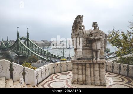 Budapest, Ungarn - 6. November 2019: Szent Istvan Kiraly, Statue des Heiligen Stephan auf dem Gellert-Hügel. Die Stadt mit Freiheitsbrücke über die Donau im Hintergrund. Skulptur. Horizontales Foto. Stockfoto