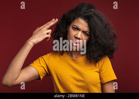 Bild von enttäuschten afroamerikanischen Frau tun Waffe Geste an ihrem Kopf mit Fingern isoliert über rotem Hintergrund Stockfoto