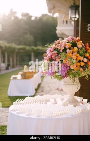Ein riesiger Strauß in einer alten Marmorvase aus rosa, roten, orangen und gelben Rosen, grünen Hortensien, lila Orchideen. Steht auf einem runden Tisch mit Karten von Meer Stockfoto