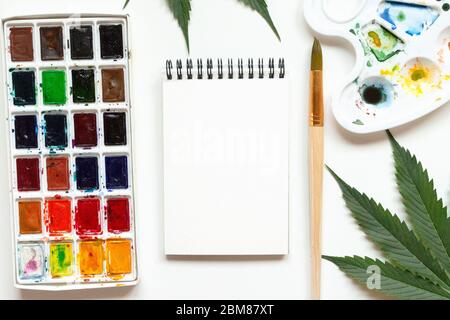 Set von Aquarellfarben, Kunstpinsel, Palette und leeres Album. Marihuana-Blatt. Cannabis offenbart Kreativität. Der Begriff der Kunst Stockfoto
