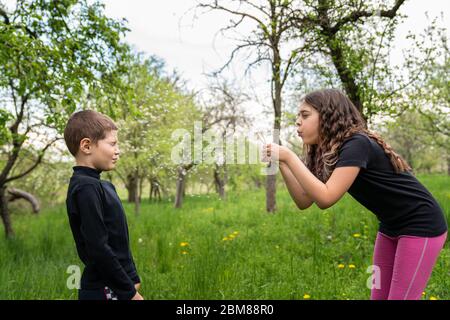 Verspielt brünette Mädchen weht auf weißen Löwenzahn auf ihre Freundin in schwarzem Hemd Stockfoto