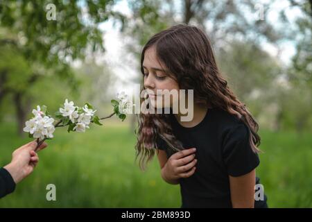 Zartes Brünette Mädchen in schwarzem T-Shirt lehnte sich in Richtung blühenden Zweig in der Hand des Jungen Stockfoto