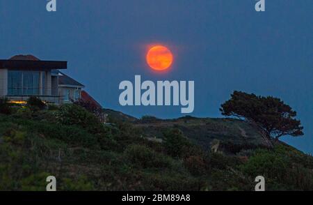 Swansea, UK,7. Mai 2020 EIN atemberaubender blutroter Mond erhebt sich heute Abend über der Skyline von Langland Bay in der Nähe von Swansea, da die Atmosphäre aufgrund der fehlenden Verschmutzung durch die aktuelle Sperrung des Coronavirus klar bleibt. Kredit: Phil Rees/Alamy Live News Stockfoto