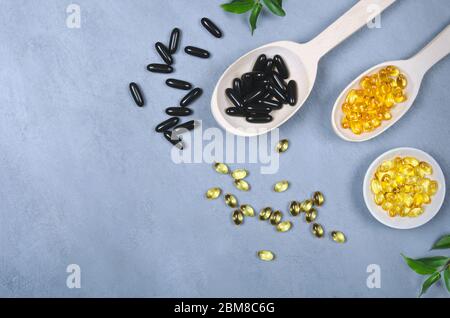 Schwarze und gelbe Pillen auf Holzlöffel auf grauem Hintergrund Stockfoto