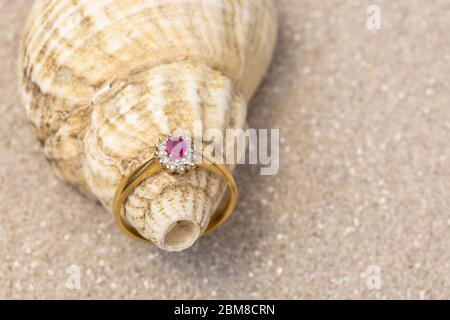 Diamant und Rubin Ehering Schmuck auf einer Schale auf Sand. Hochzeitskonzept am Strand Stockfoto