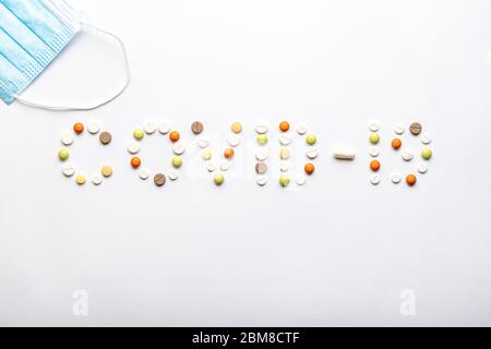 Covid-19 Inschrift mit Pillen und Kapseln und eine blaue Einweg-medizinische Schutzmaske flach lag auf einem weißen Hintergrund Kopierraum. Coronavirus Stockfoto