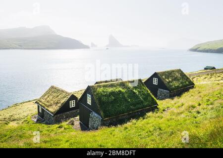 Malerischer Blick auf die traditionellen färöischen Grashäuser im Dorf Bour. Drangarnir und Tindholmur Meer stapeln sich im Hintergrund. Vagar-Insel, Färöer, Dänemark. Landschaftsfotografie