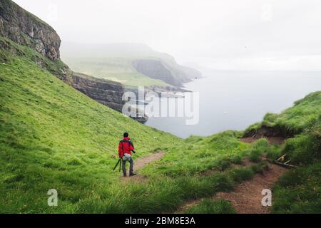 Neblige Ansicht der Insel Mykines mit Touristen in roter Jacke auf den Färöer Inseln, Dänemark. Landschaftsfotografie Stockfoto