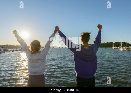 Rückansicht des glücklichen jungen multi ethnischen Paar mit Fäusten zusammen am Pier im Freien angehoben Stockfoto