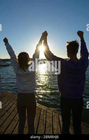 Rückansicht des glücklichen jungen multi ethnischen Paar mit Fäusten zusammen am Pier im Freien angehoben Stockfoto