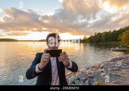 Junger Geschäftsmann, der mit dem Handy in schöner landschaftlich schöner Küste fotografiert Stockfoto