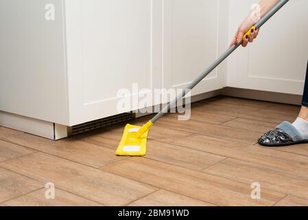 Eine junge Frau wäscht Holzböden aus einem Laminat in einer hellen Küche. Das Mädchen wäscht Staub und Schmutz unter dem Küchenschrank. Stockfoto