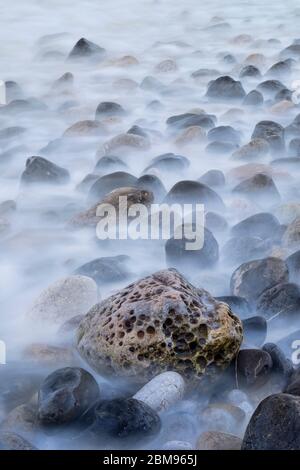 Langzeitbelichtung von Gesteinen, die von der Flut überspült werden, Penmon, Anglesey, North Wales, Großbritannien Stockfoto