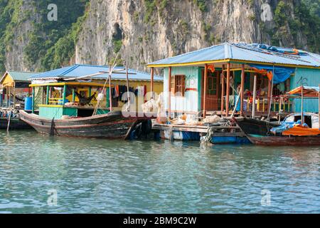 Halong Bay Vietnam - Oktober 21 2013; bunte Häuser von Fischern Menschen über Wasser gegen Felswände mit Fischerbooten gebunden alonside gebaut. Stockfoto