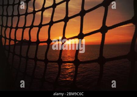 Sonnenuntergang über der Insel Rakata, dem Vulkan Anak Krakatau und der Insel Panjang auf der Sundastraße, fotografiert durch eine Jakobsleiter (Marineleiter) an Bord des KRI (indonesisches Marineschiff) Arun. Archivbild. Stockfoto