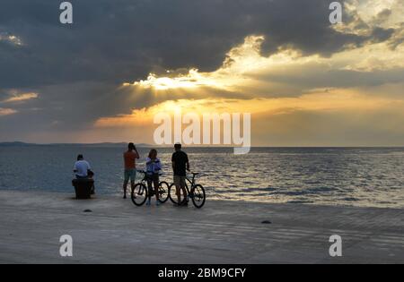 Touristen genießen den Sonnenuntergang über der Adria von der Promenade in Zadar, Kroatien. Stockfoto